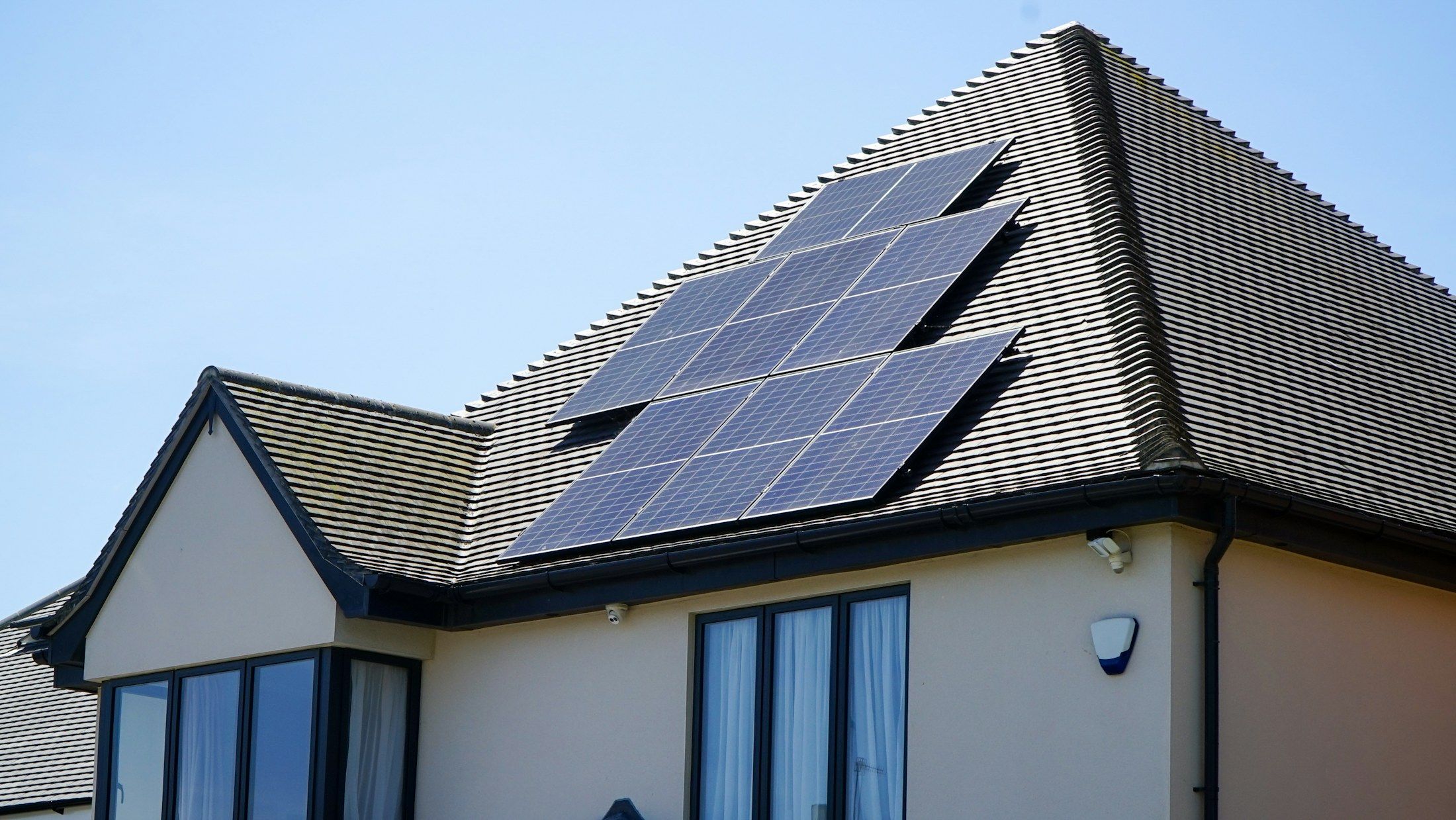 Solar panels on the tiled roof of a two-storey house under a clear blue sky