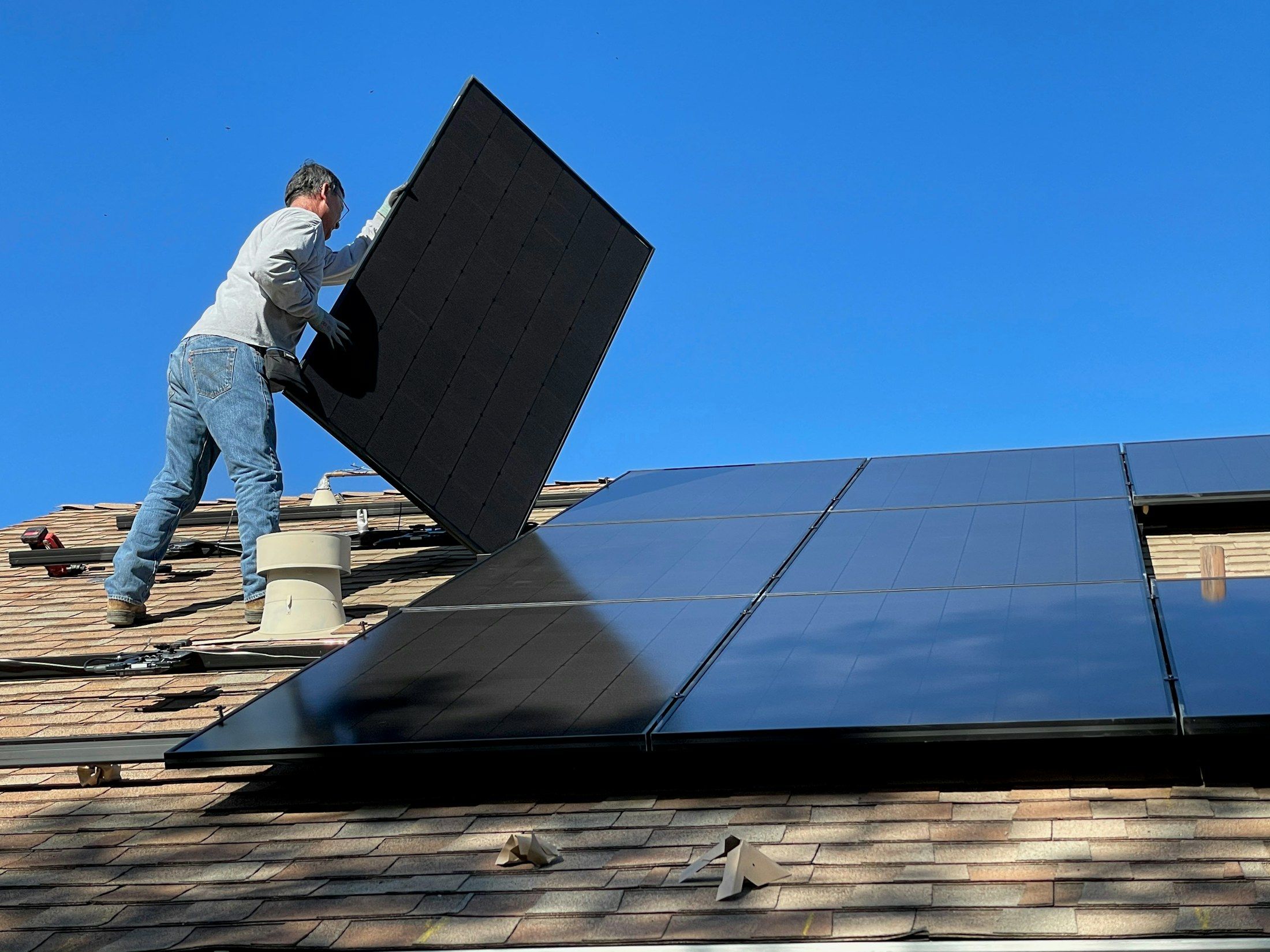 An installer lifts a black solar panel into place on a roof